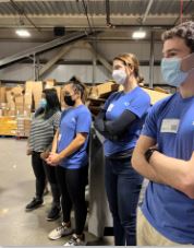 4 people standing in a line in warehouse with covid masks on