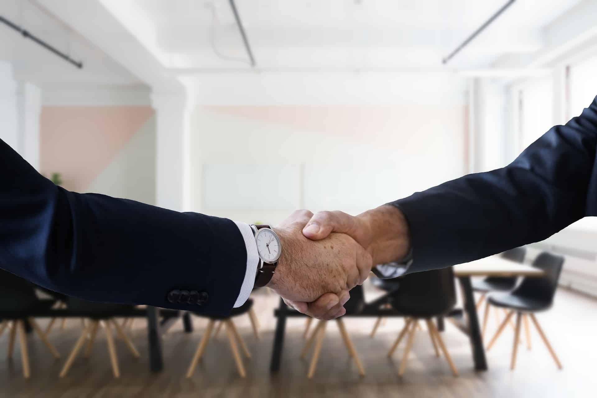 two hands shaking in foreground of conference room